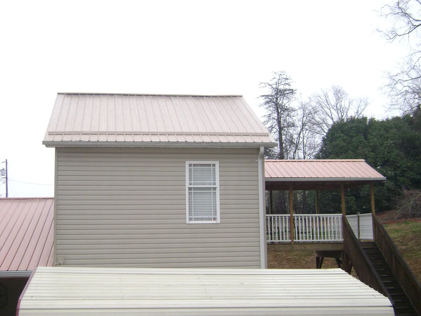 Tan metal roofs on a two story addition and attached porch, from a Roof Replacement job in Davenport
